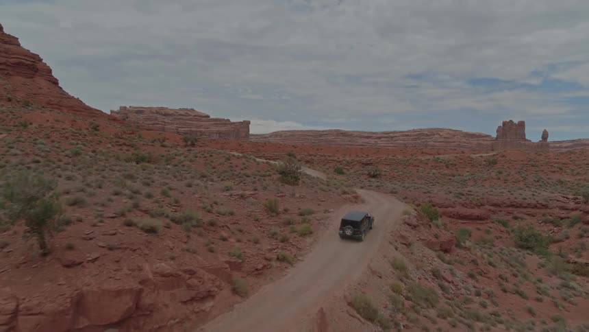 Jeep drives on dirt road around large rock formation in desert