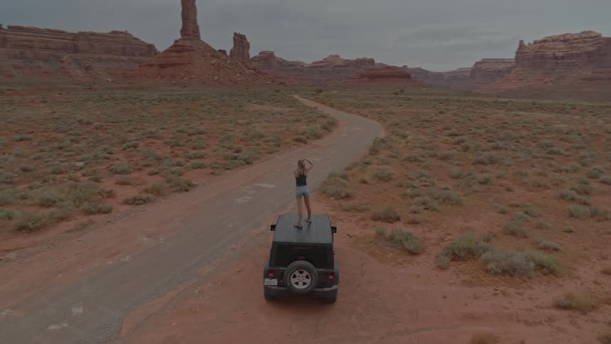 A person standing on a jeep in the desert taking pictures