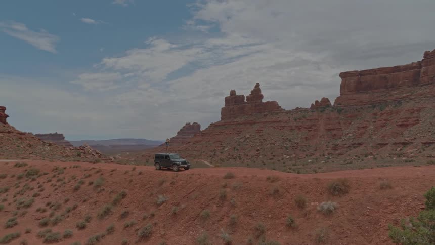 A traveler stands on the roof of a parked car in a desert
