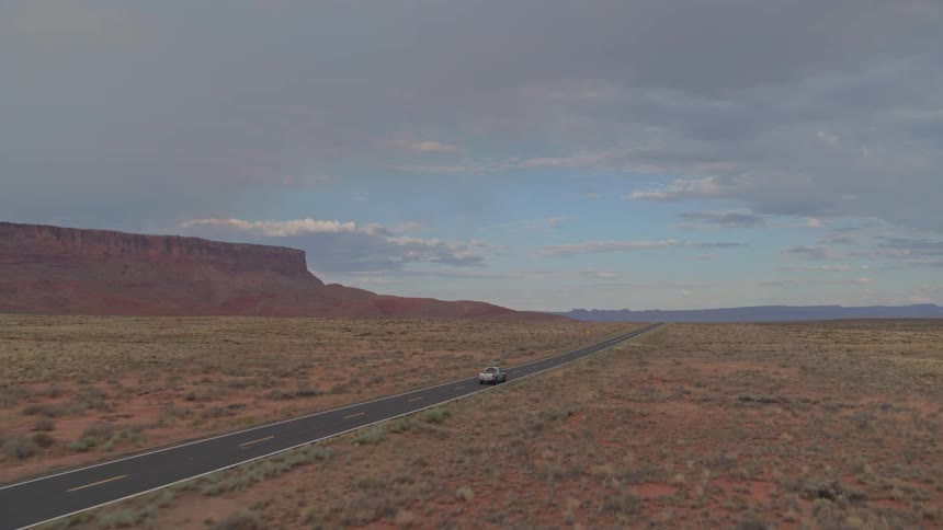 A truck driving down a long flat highway in the desert