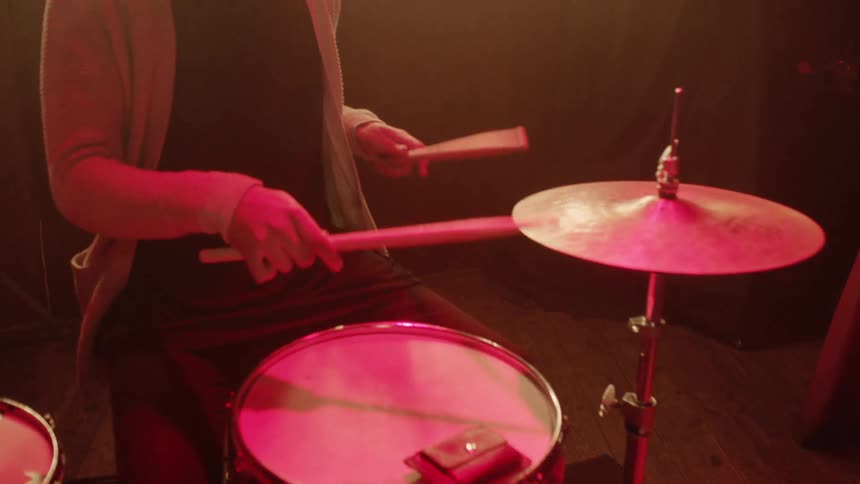 Man with two sticks plays drums in red dim light