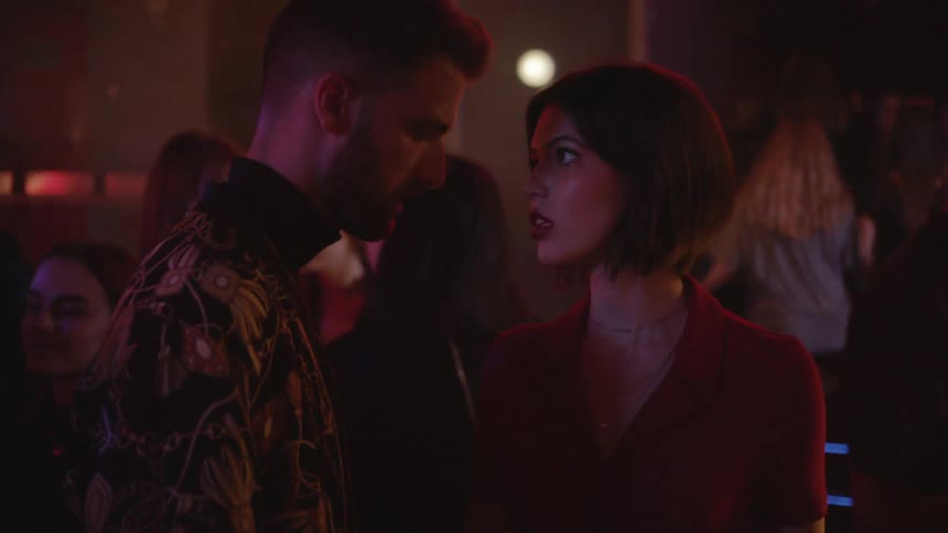 A man approaches a woman at a club and starts to kiss her before he is pulled away