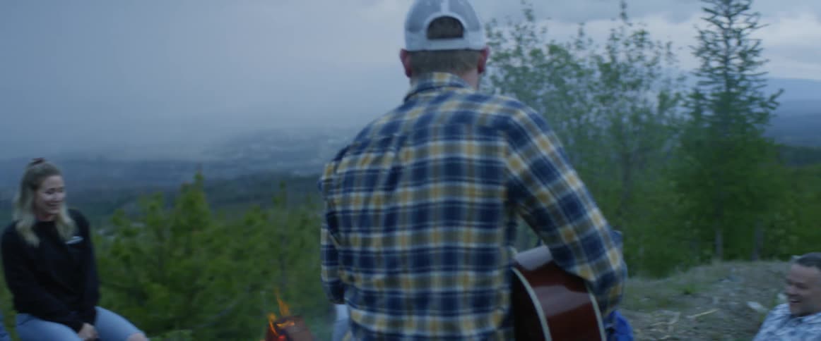 People are outside around a fire while a man plays guitar
