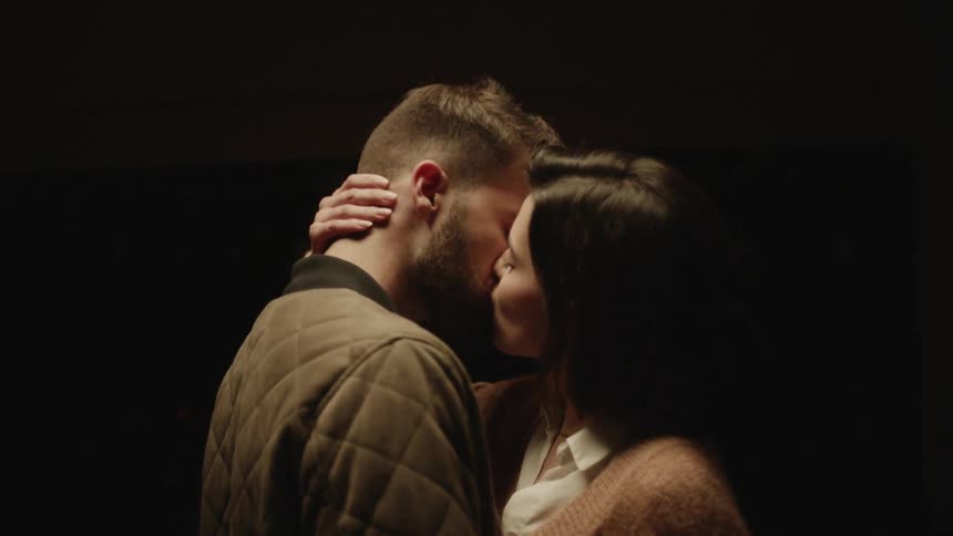 A couple meets together under a light in the dark and kisses