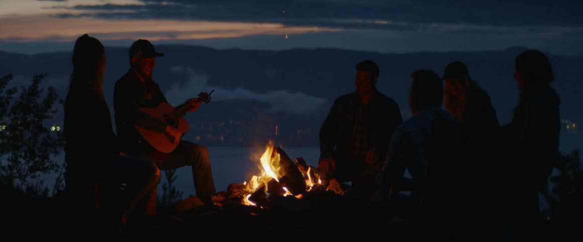 A man plays guitar for others at a campfire