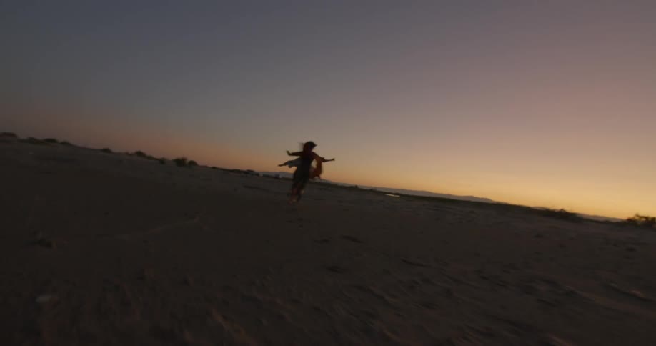 Two people are running and spinning around on a windy beach