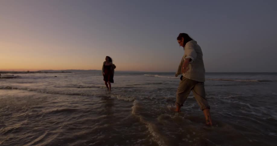 People are by the beach in the water at dusk