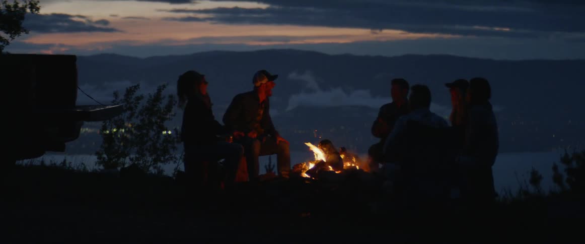 Group of people sit around a campfire as the sun sets