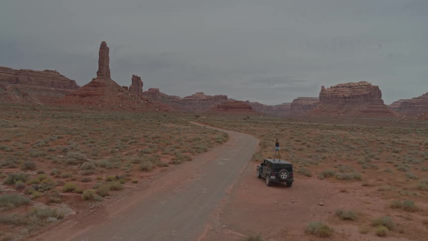 A traveler stands on the roof of a parked car in a desert