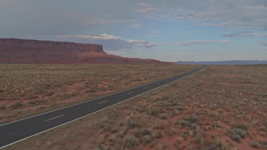 A long flat highway in the desert surrounded by red rocks
