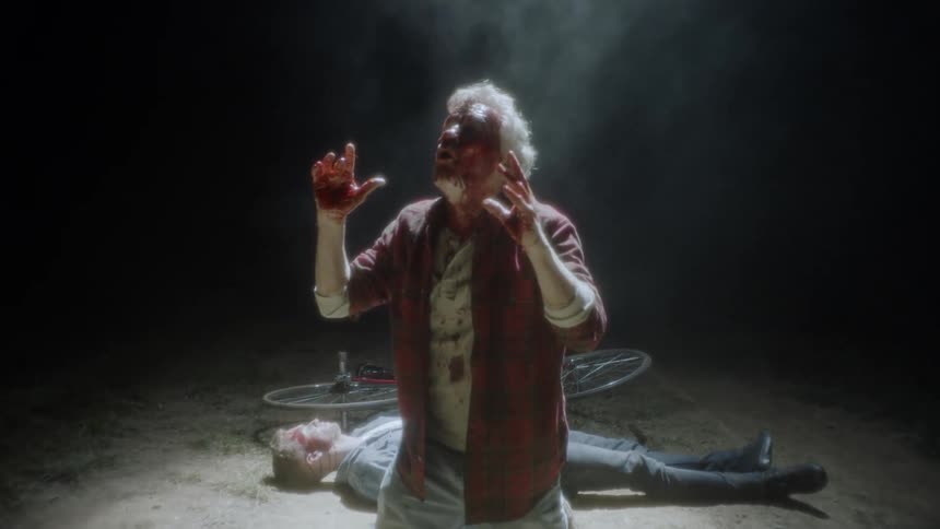 A bleeding man kneels in front of a body and bicycle