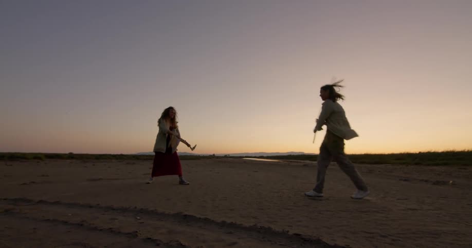 Two people swing sticks at each other on the beach