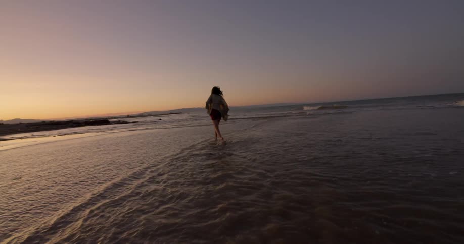 A woman is running in the tide at sunset