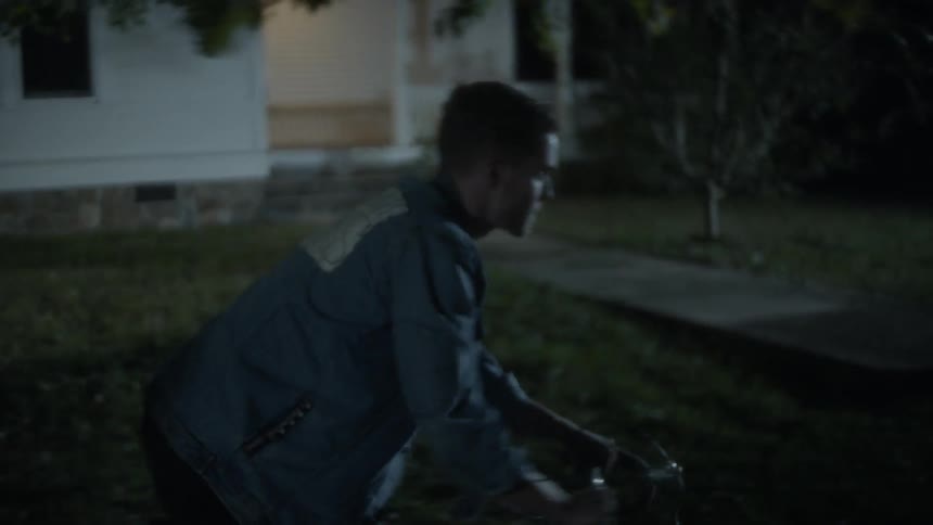A man rides a bike in a neighborhood at night