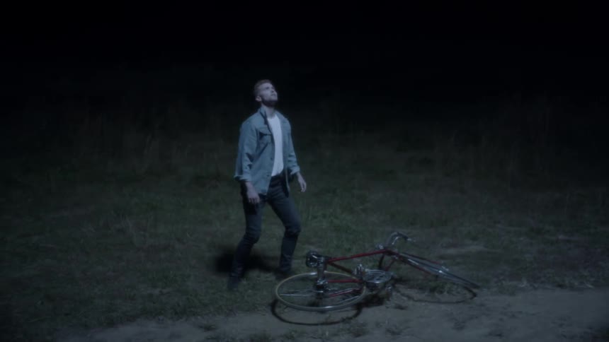 A man riding a bike hops off and looks at the sky