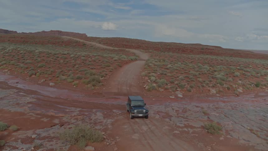 A four wheel drive car makes its way across a wet and dirty path cutting through shrubbery