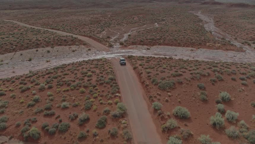 Red dirt and shrubs with a vehicle driving down a rough road