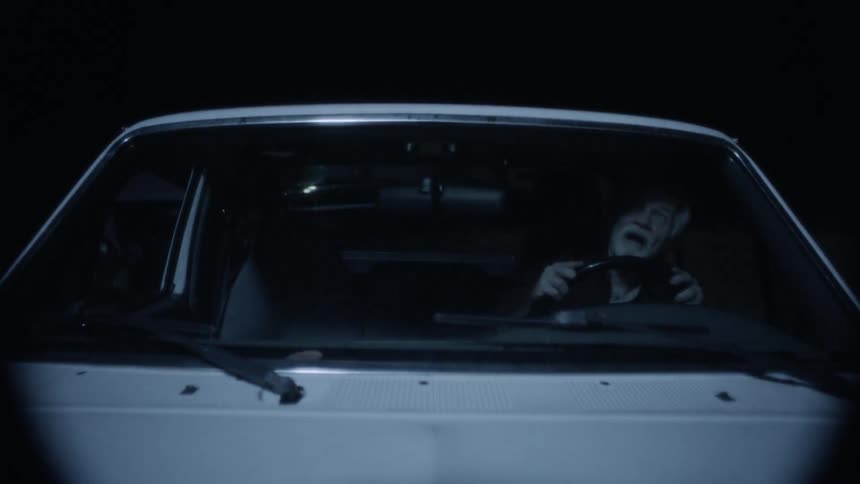 An elderly man is driving in a car and looking up into the sky