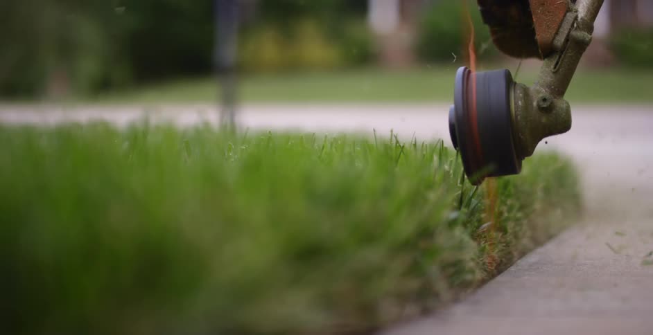 A person is cutting grass by a sidewalk