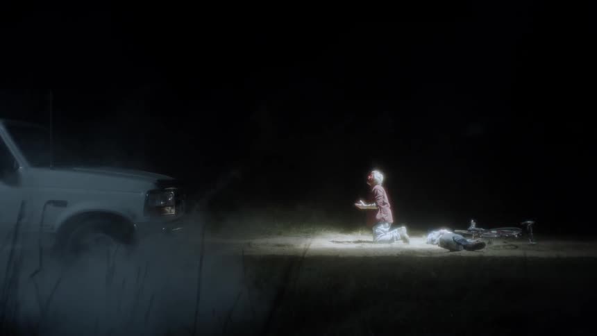 A person is outside sitting on the ground by a truck