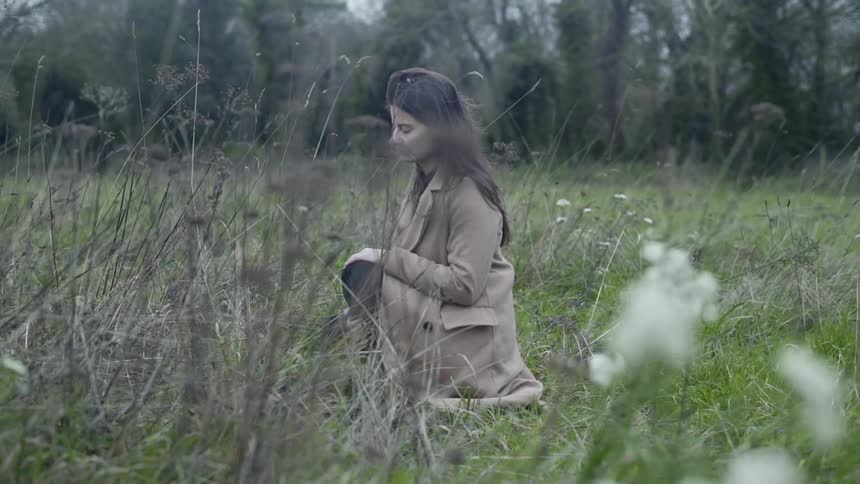 White woman relaxes in a field on a overcast windy day