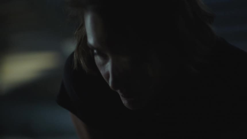 A woman standing in a dark room looks down at the ground then looks up again