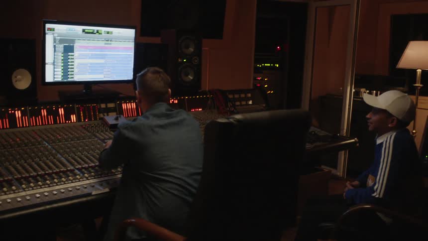 A few men in a music studio laugh and work