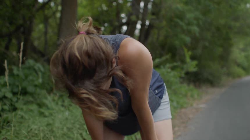 Woman jogging down a wood lined path and stopping to catch her breath