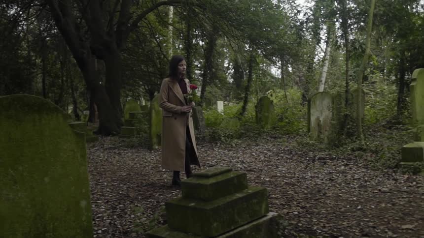 A woman walks through a cemetery while carrying a rose