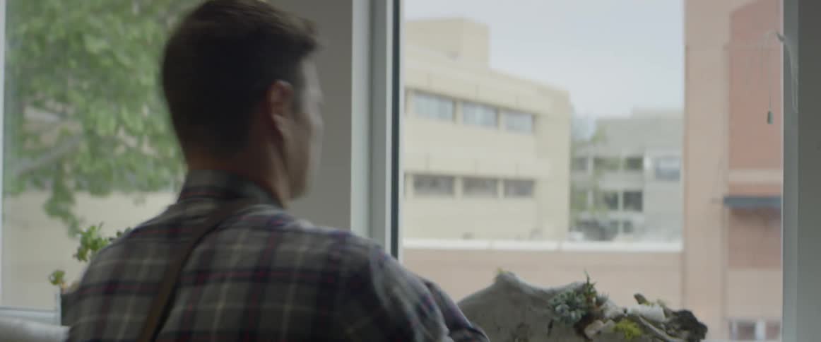 A man puts a satchel over his shoulder and gets up from a table by a window