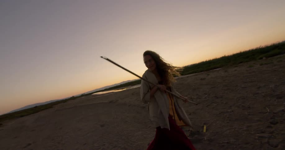 Two women play on the sand at sunset as one holds a long stick