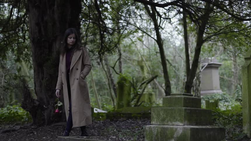 A woman walks through the cemetery carrying a flower