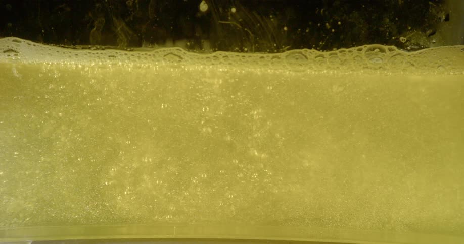 Yellow liquid sloshes around in a container with bubbles rising to the surface