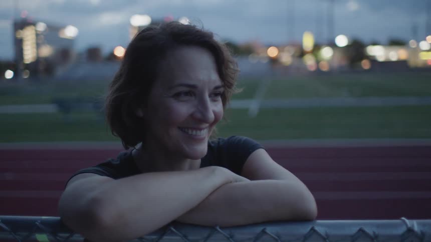 A woman leaning on a fence next to a track field