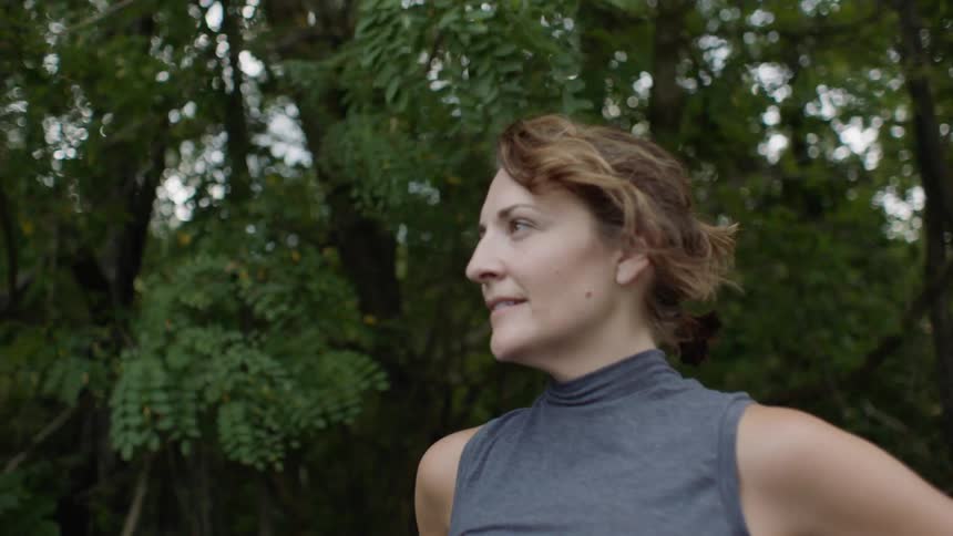 A woman in a wooded outside area who is looking ahead and smiling