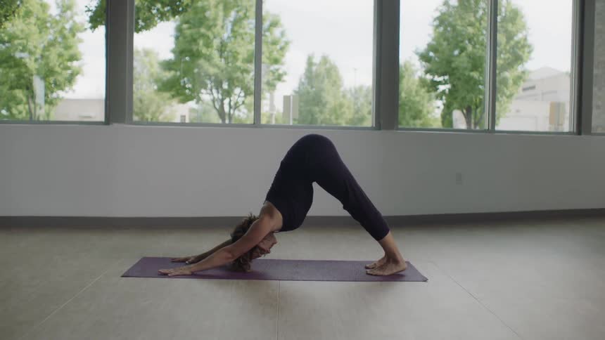 Woman doing yoga on a mat in a large room with windows