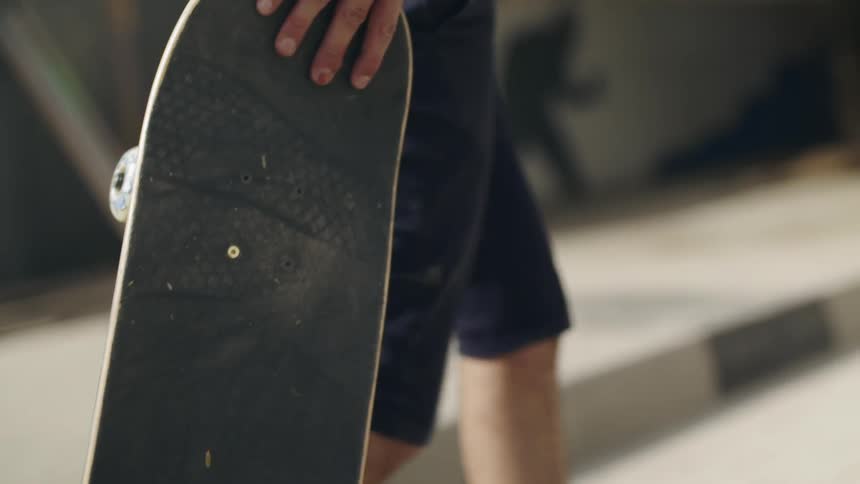 A man walks along carrying his skateboard