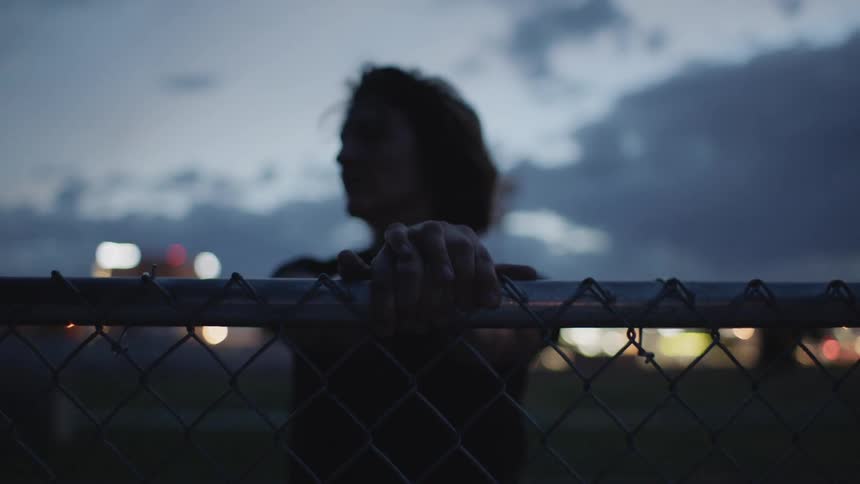 Person leans on fence at dusk