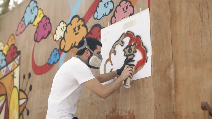 A man spray paints over a stencil on an outdoor wall