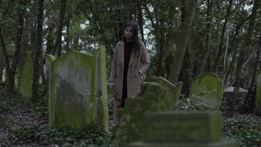 A woman stands near a gravestone full of moss