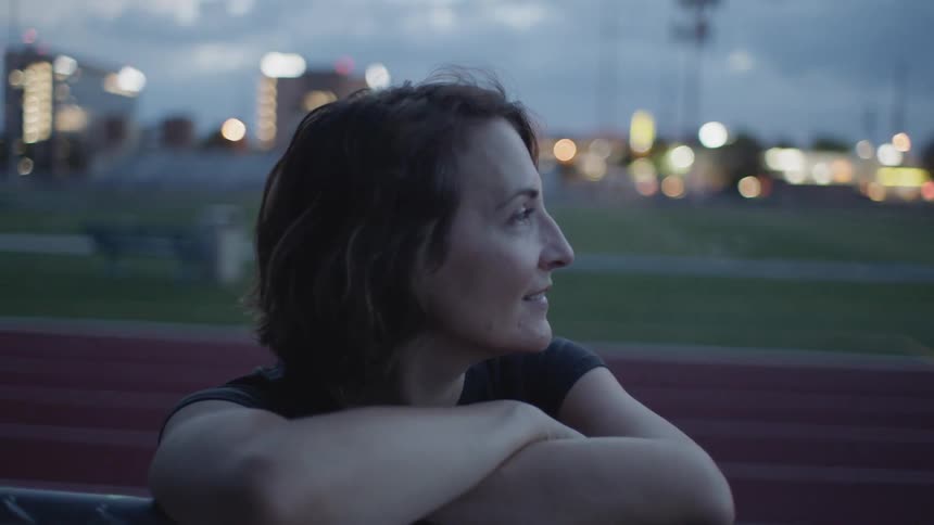 A woman leans on the fence smiling by the track