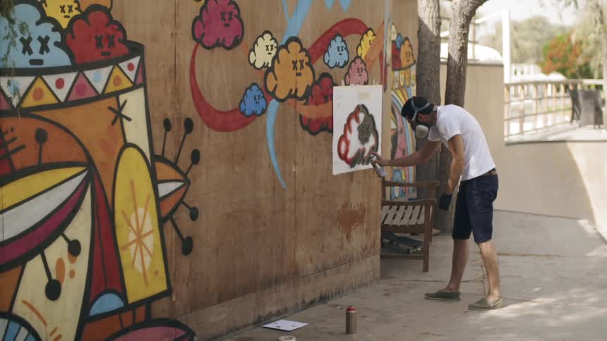 An artist paints the side of a building using spray paint and stencils
