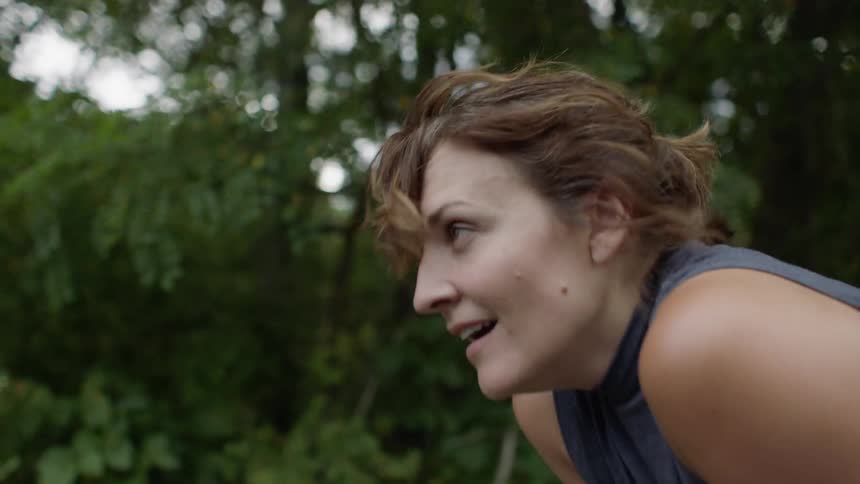 A woman jogging then stopping to rest in a wooded area