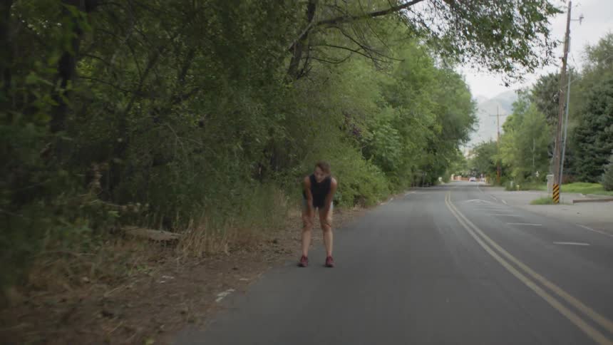 A woman jogs near the forest and stops to breathe for a second