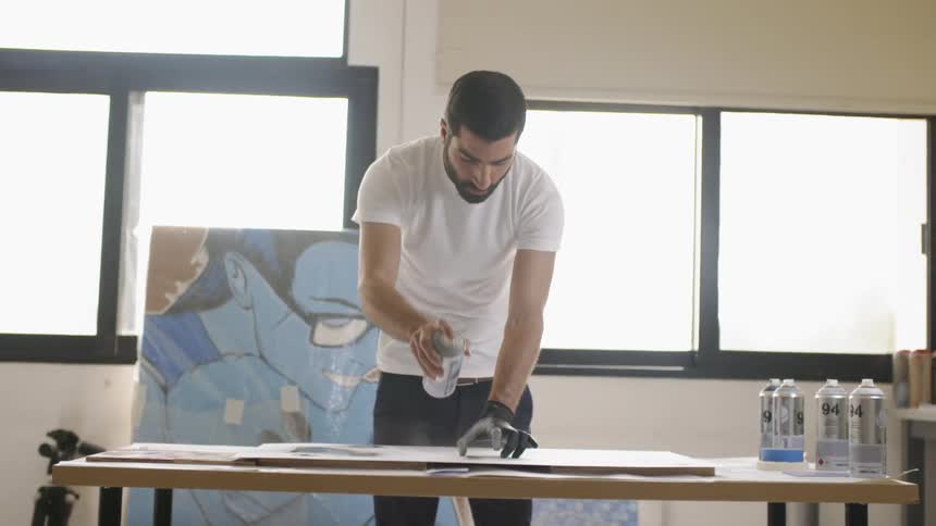 A man spray painting on a canvas placed on a table