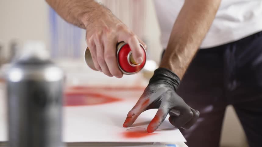 A man spray painting while he holds an object wearing gloves