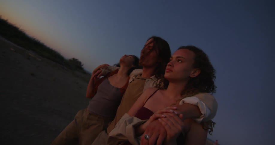 A man walks between two women with his arms around both at sunset