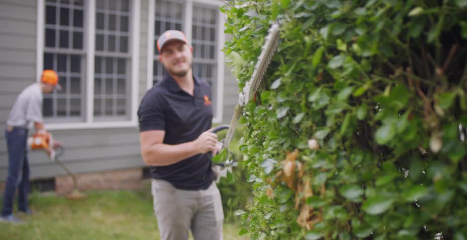 A man is cutting hedges with a trimmer