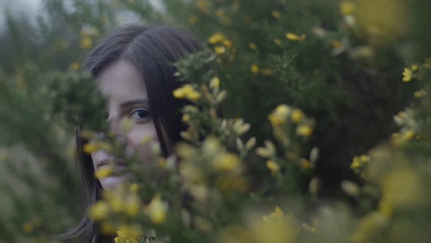 Woman standing behind green and yellow shrubbery