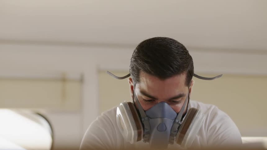 A man wears a face mask while spray painting indoors
